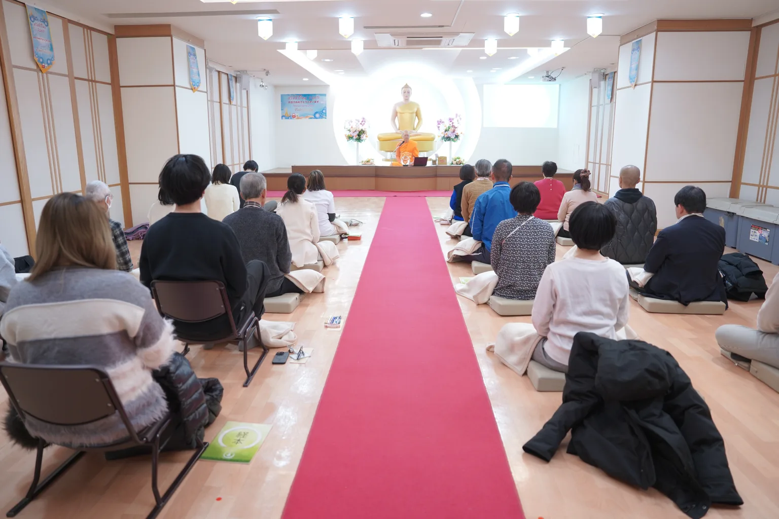 Wide rear view of participants meditating together in the main hall